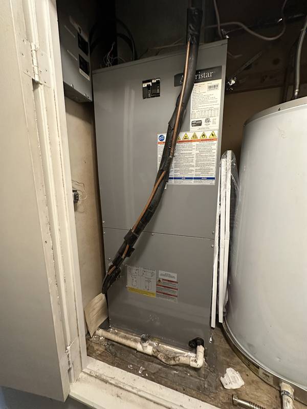 Air handler in a utility closet next to a water heater, with refrigerant and drain lines