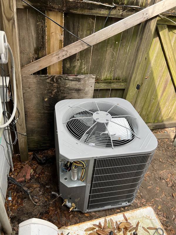 Outdoor condenser beside a wooden fence with its service panel open